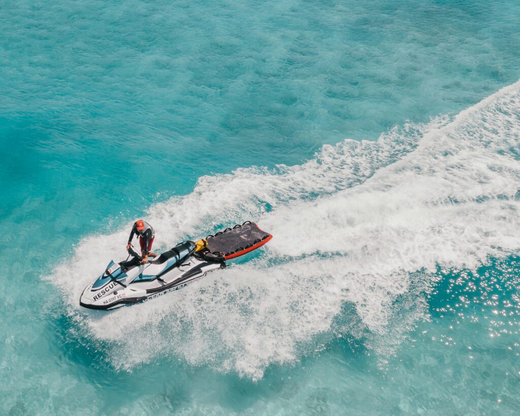 Jetski performing rescue operation on vibrant blue Hawaiian waters from an aerial perspective.